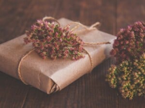 Homemade Gift box wrapped in kraft paper and pink Sedum flowers on wooden table.