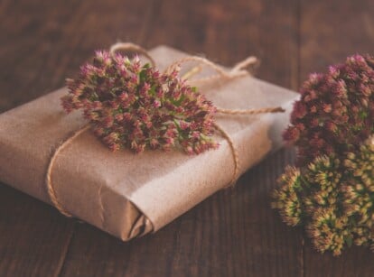 Homemade Gift box wrapped in kraft paper and pink Sedum flowers on wooden table.