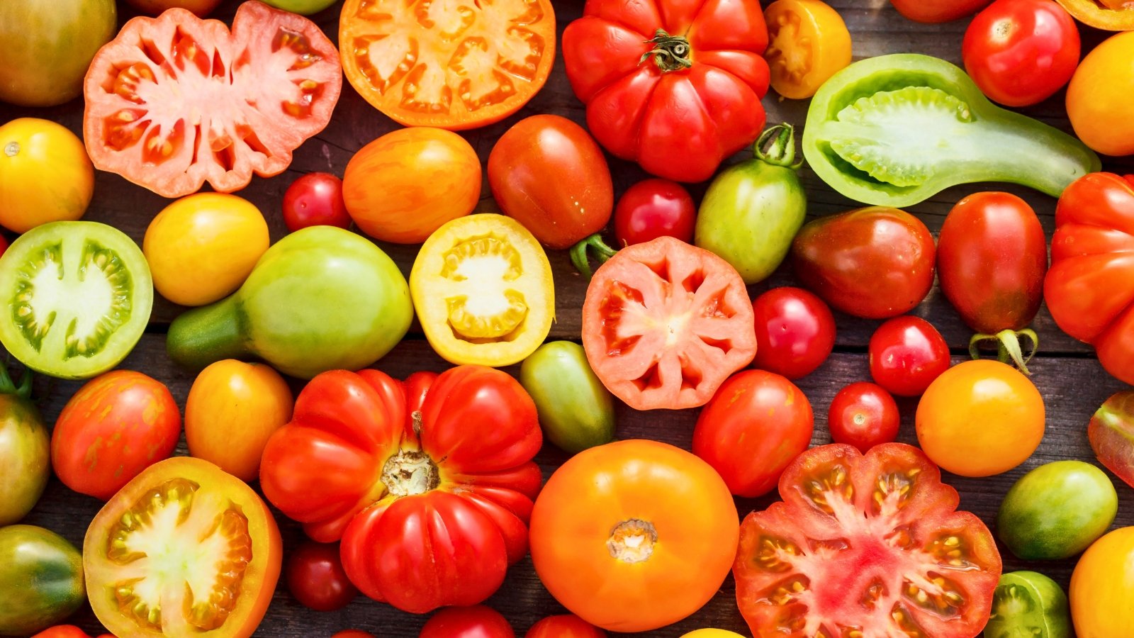 A variety of tomatoes, some halved, some whole, arranged on a sunlit table, showcasing vibrant colors and textures, inviting the viewer to savor the diversity of nature's bounty.